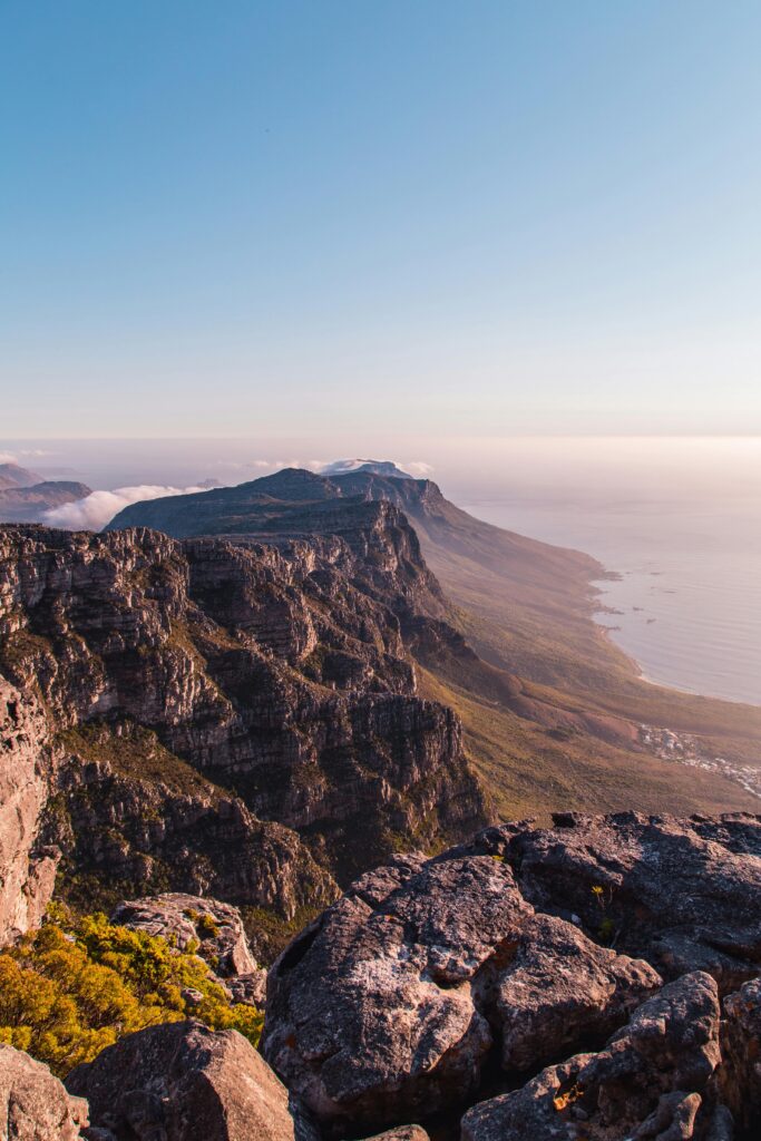 A panoramic view of Table Mountain’s rugged cliffs and flat summit under a clear blue sky, with the coastline and ocean stretching into the distance below—perfect for exploring our latest specials on local tours.