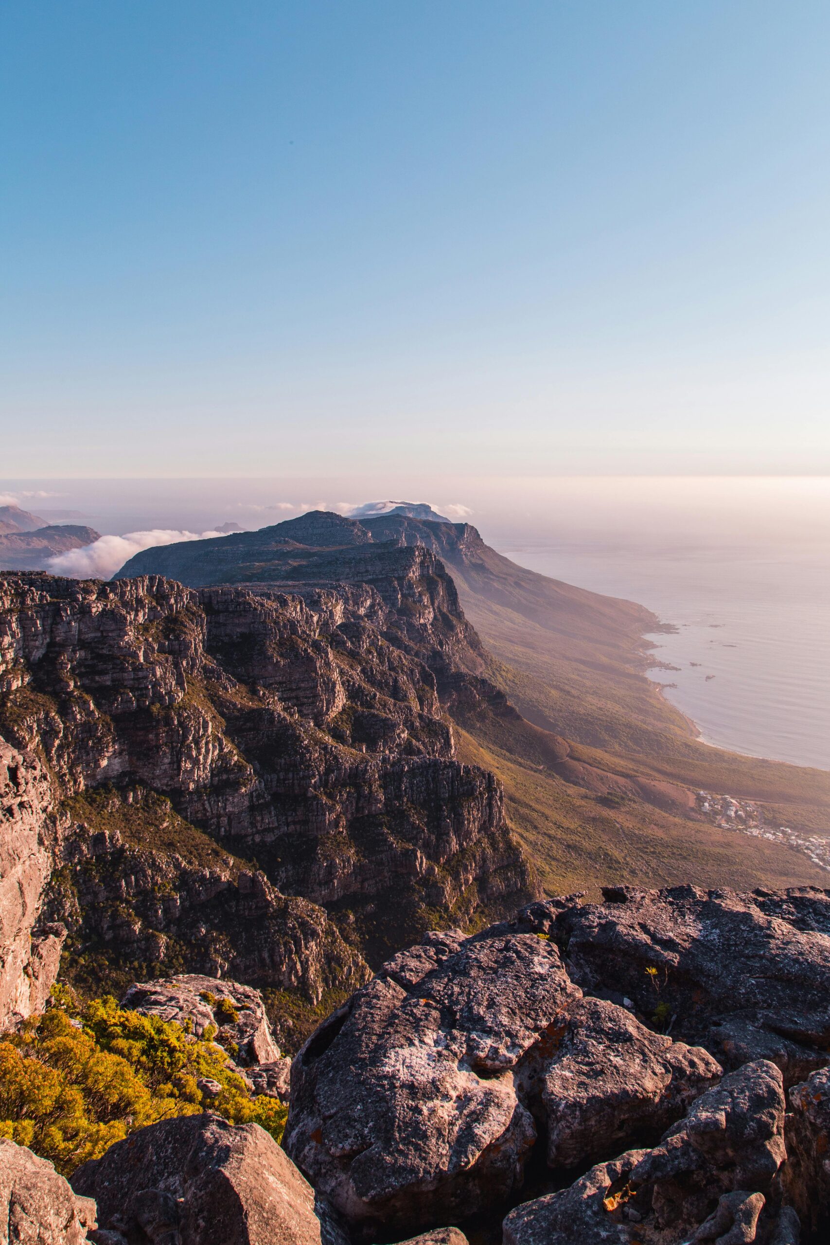 A panoramic view of Table Mountain’s rugged cliffs and flat summit under a clear blue sky, with the coastline and ocean stretching into the distance below—perfect for exploring our latest specials on local tours.