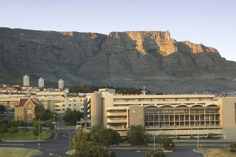 The Cape Peninsula University of Technology campus, with modern and historic buildings, sits in front of a large, rocky mountain under a clear sky at sunset.