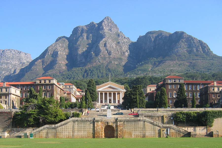 The University of Cape Town’s main campus, with its iconic columned building, is surrounded by historic structures and greenery, all set against the breathtaking backdrop of Table Mountain under a clear blue sky.